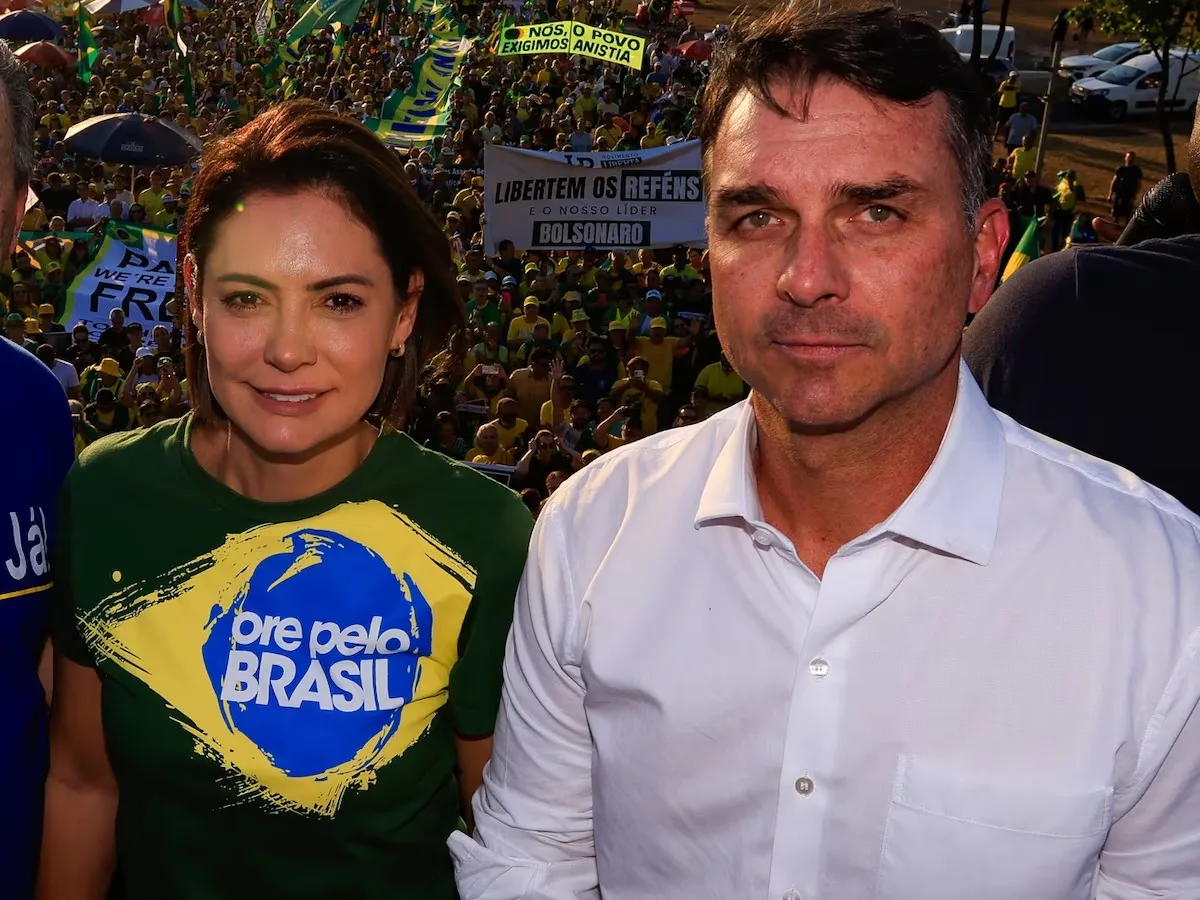 A ex-primeira-dama Michelle Bolsonaro e o senador Flávio Bolsonaro olhando para a câmera, ela sorrindo
