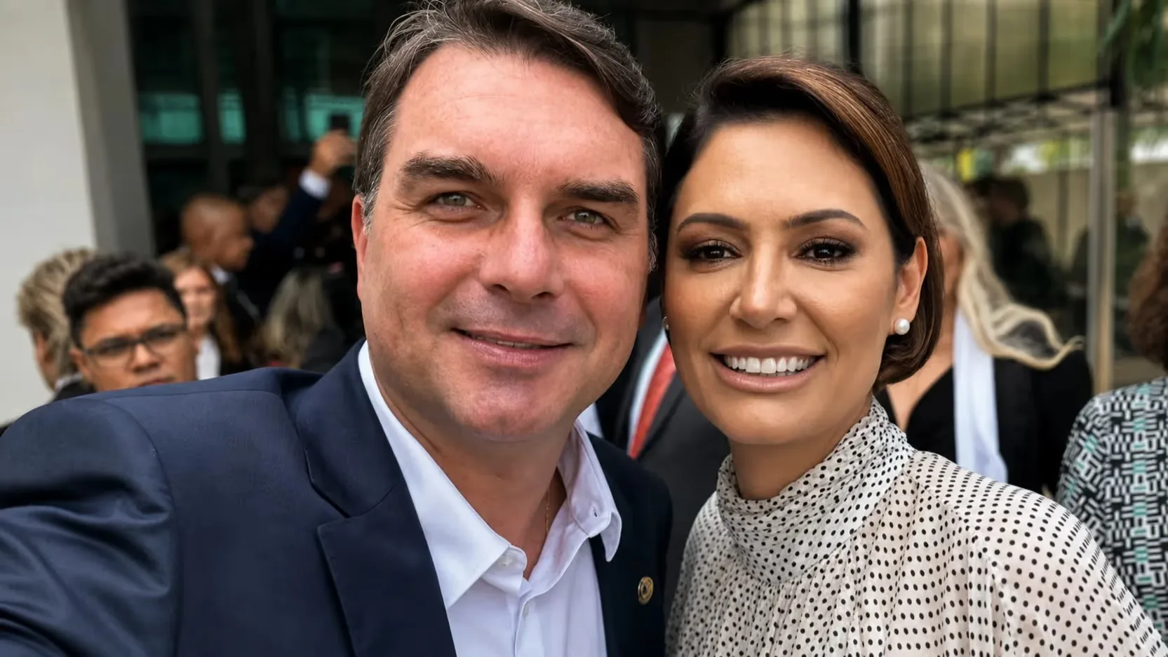 Flávio Bolsonaro e Michelle Bolsonaro sorrindo para selfie, em close, lado a lado