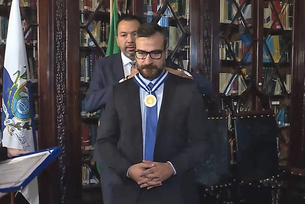 O deputado Márcio Canella (União) coloca a Medalha Tiradentes no delegado Marcus Amim, ex-secretário de Polícia Civil do Rio de Janeiro - Reproduçao/ TV Alerj