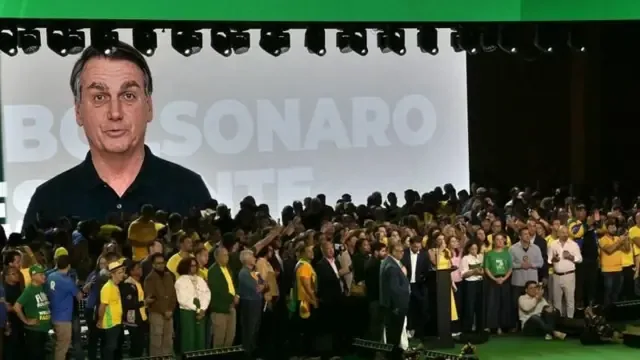 Telão mostra Bolsonaro falando, enquanto partidários se reúnem no palco